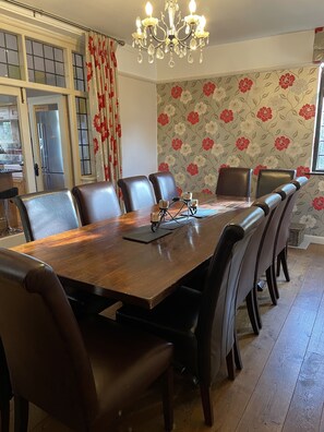 Ein Esszimmer mit Holztisch, sechs Stühlen, einer Chandelierleuchtre und floraler Tapete.