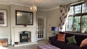 A living room with a fireplace, a sofa, a matching ottoman, a chandelier, and a large window with curtains. - Striking home IN Stratford-on-Avon, a stroll to all key attractions.Sleeps 14-15 (Stratford-upon-Avon)