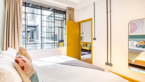 Hotellihuone, jossa on suuri sänky, ikkuna verhoilla, keltainen ovi ja näkymä kaupungin ylle.