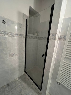 Ducha con mampara de vidrio, pared con azulejos y ducha de esquina.