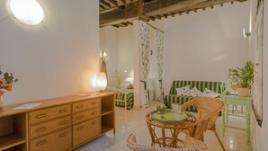A cozy room with a wooden desk, wicker chairs, a green-striped sofa, and a small table with a plant.