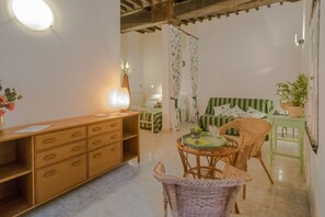 A cozy room with a wooden desk, wicker chairs, a green-striped sofa, and a small table with a plant.