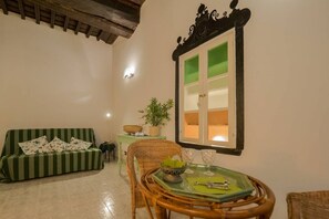 A cozy living room with a green-striped sofa, a wicker chair, a glass table with a green placemat, and a window with a green view.