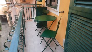 A balcony with a green table and chairs, a window, and a door with a shutter.