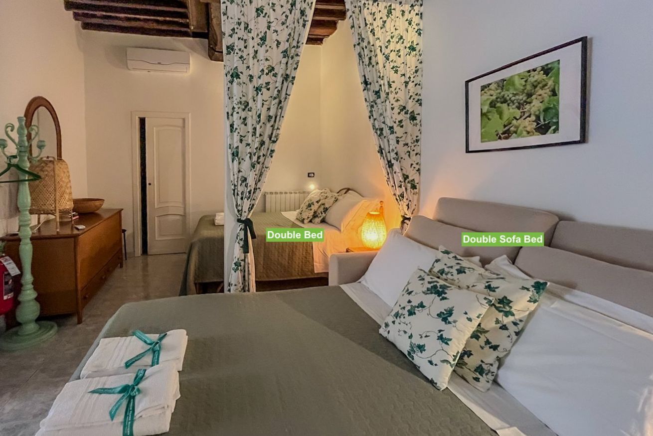 Una cama doble y un sofá cama doble en una habitación con cortinas florales, un cuadro en la pared y una lámpara de noche.