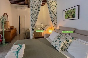 A double bed and a double sofa bed in a room with floral curtains, a framed picture on the wall, and a bedside lamp.