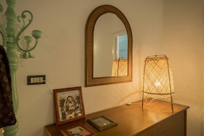 A room with a wooden dresser, a mirror, a framed picture, and a standing lamp. - Picabon Apartment with AC Balcony (Monterosso al Mare)