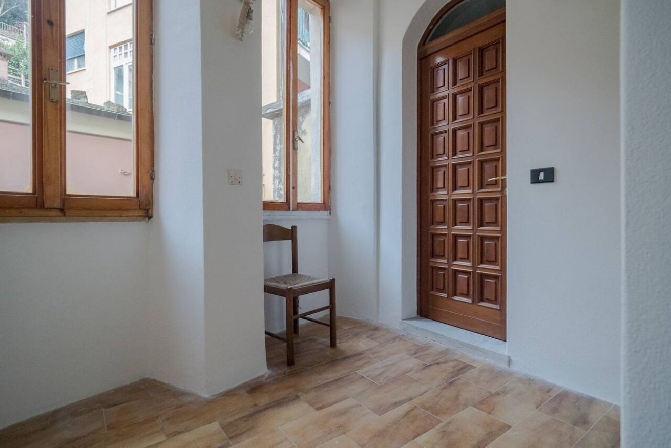 Un pasillo con puerta de madera, ventana y una silla.