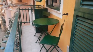 A small outdoor seating area with a green metal table and chairs, a metal bench, and a yellow wall. - Picabon Apartment with AC Balcony (Monterosso al Mare)