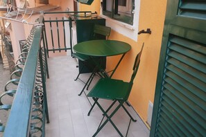 A small outdoor seating area with a green metal table and chairs, a metal bench, and a yellow wall.