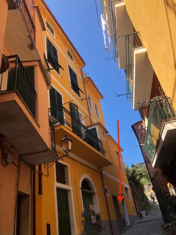 A narrow street with yellow buildings, balconies, and a clear blue sky.