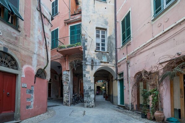 A narrow alleyway with stone buildings, arched doorways, and a red door on the left.