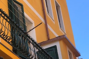 A yellow building with green shutters and a metal balcony railing.