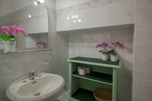 A bathroom with a white sink, green shelves, and pink orchids.