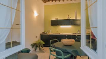 Una cocina compacta con una pared verde, una zona de comedor con mesa y sillas, y un ventanal con cortinas.