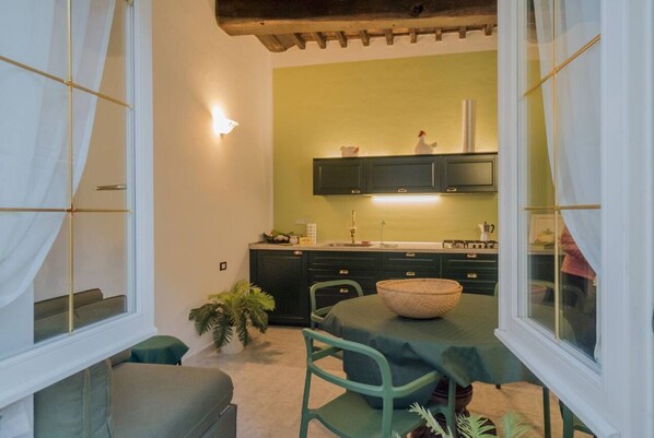 A compact kitchen with a green wall, a dining area with a table and chairs, and a window with curtains.