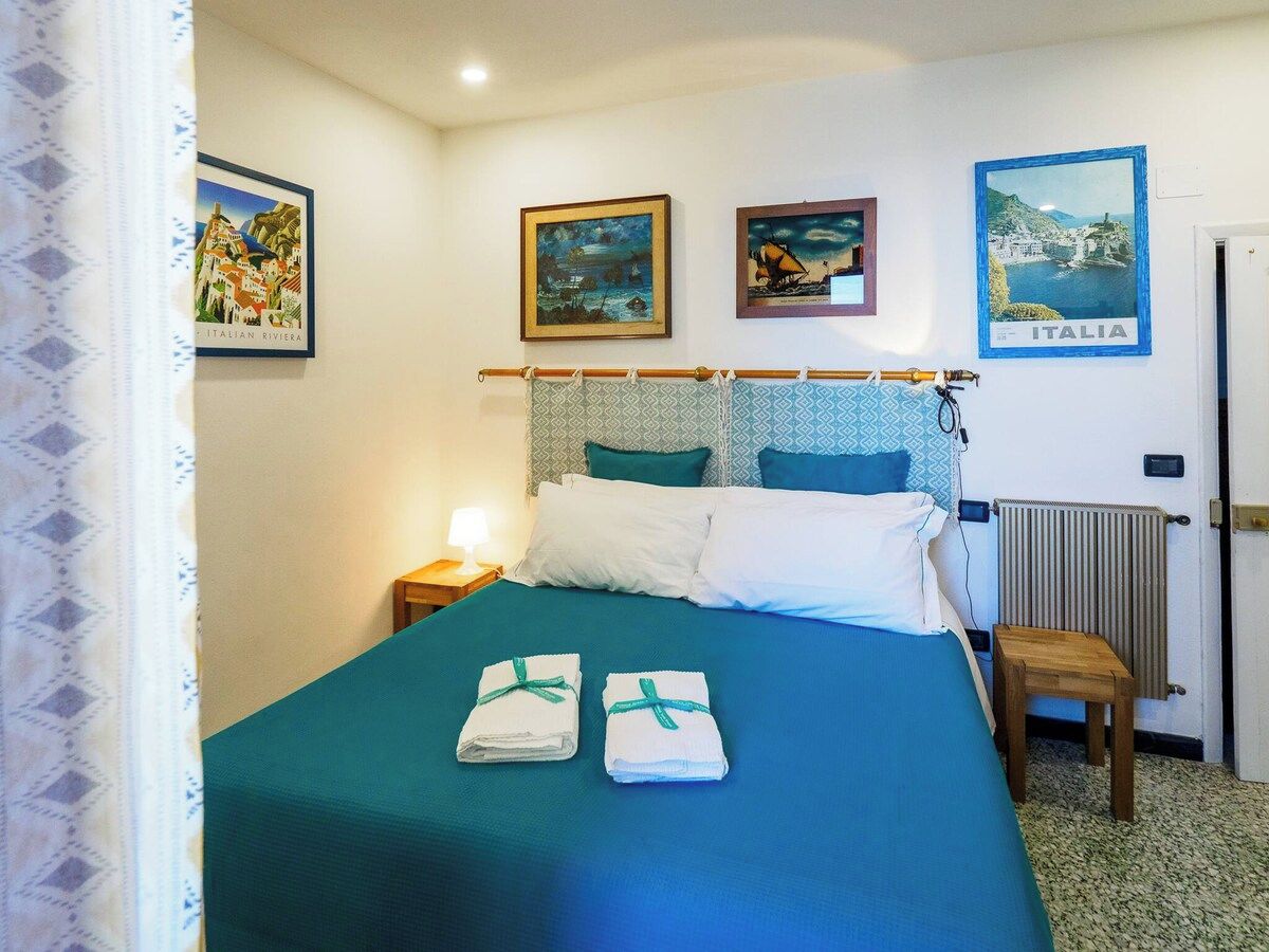 A hotel room with a bed, a nightstand, a lamp, a radiator, and three framed pictures on the wall.