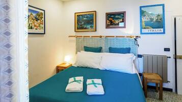 A hotel room with a bed, a nightstand, a lamp, a radiator, and three framed pictures on the wall.