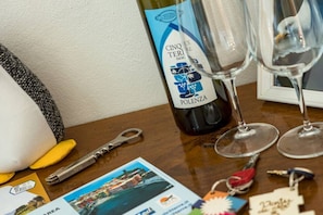 A bottle of Cinque Terre DOC wine, two wine glasses, a key, a pen, and a postcard on a wooden table.