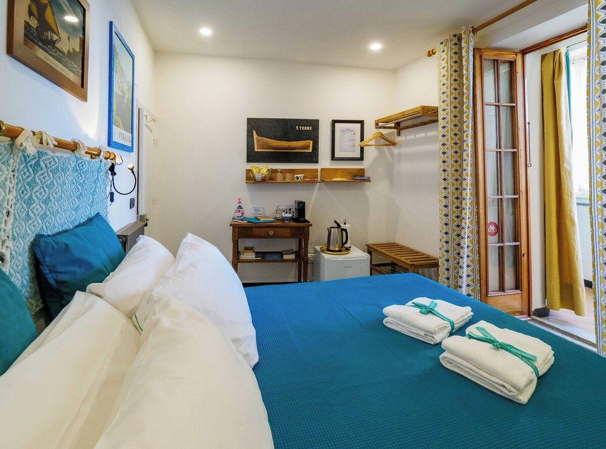 Una camera d'albergo con un letto, una scrivania con un bollitore, un piccolo tavolino e una finestra con tende.