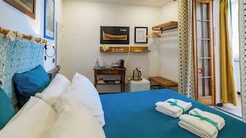 Una camera d'albergo con un letto, una scrivania con un bollitore, un piccolo tavolino e una finestra con tende.