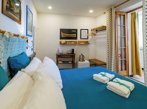 Habitación de hotel con cama, escritorio con tetera, una mesita y ventana con cortinas.