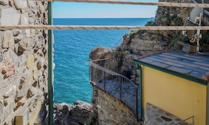 Un bâtiment situé sur la côte, doté d’un mur en pierre, d’une rambarde en métal et offrant une vue sur la mer.