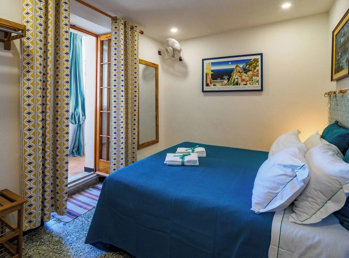 A hotel room with a bed, a painting, and a view of the outside.