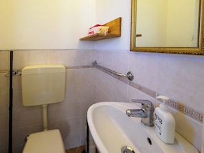 Un baño con inodoro, lavamanos y un estante con artículos de aseo.
