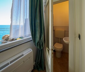 A bathroom with a toilet, sink, and a window with a view of the sea.