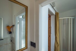 Un baño con un espejo grande, una ducha con cortina y un enchufe a la vista.