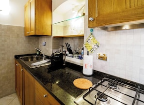 A kitchen with wooden cabinets, a granite countertop, a gas stove, and a stainless steel sink. - Ventu de Ma First Floor Studio with AC (Vernazza)