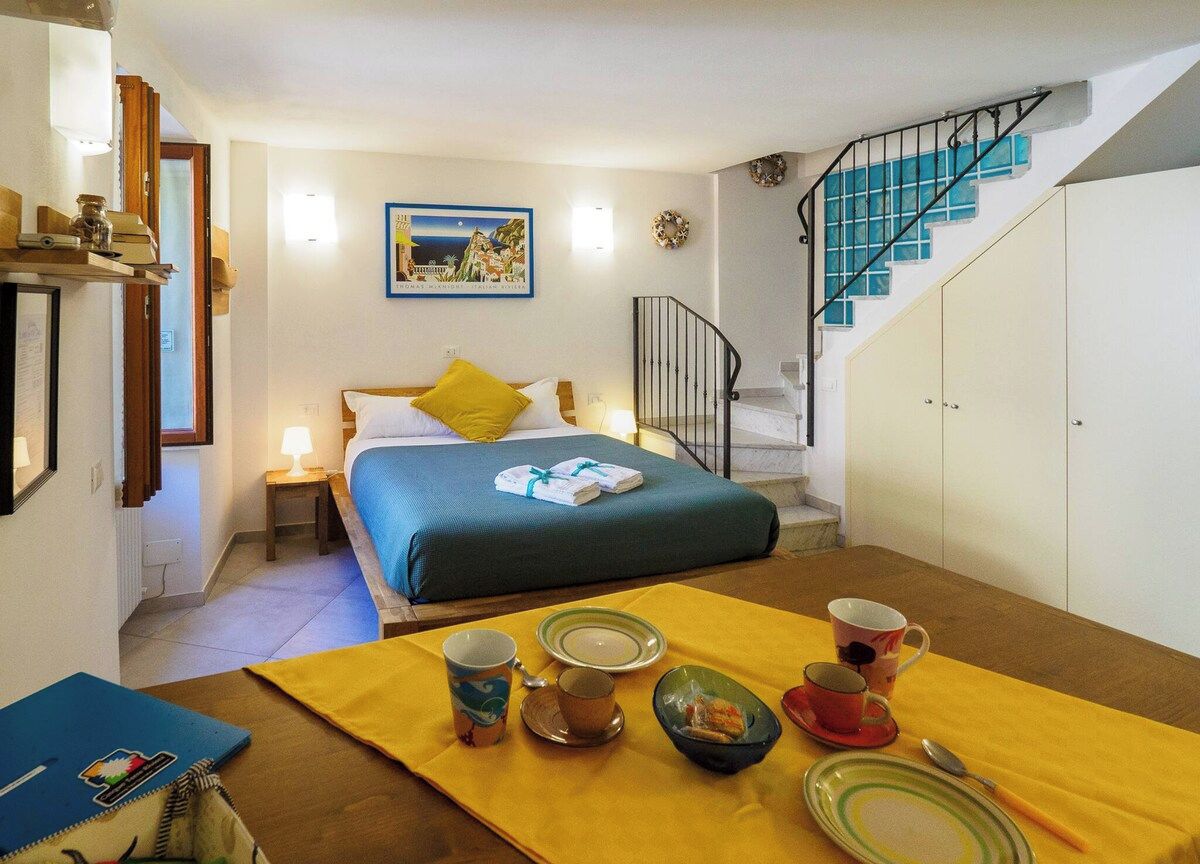 Habitación de hotel con una cama, una mesa de comedor con alimentos para el desayuno, una escalera y un cuadro en la pared.