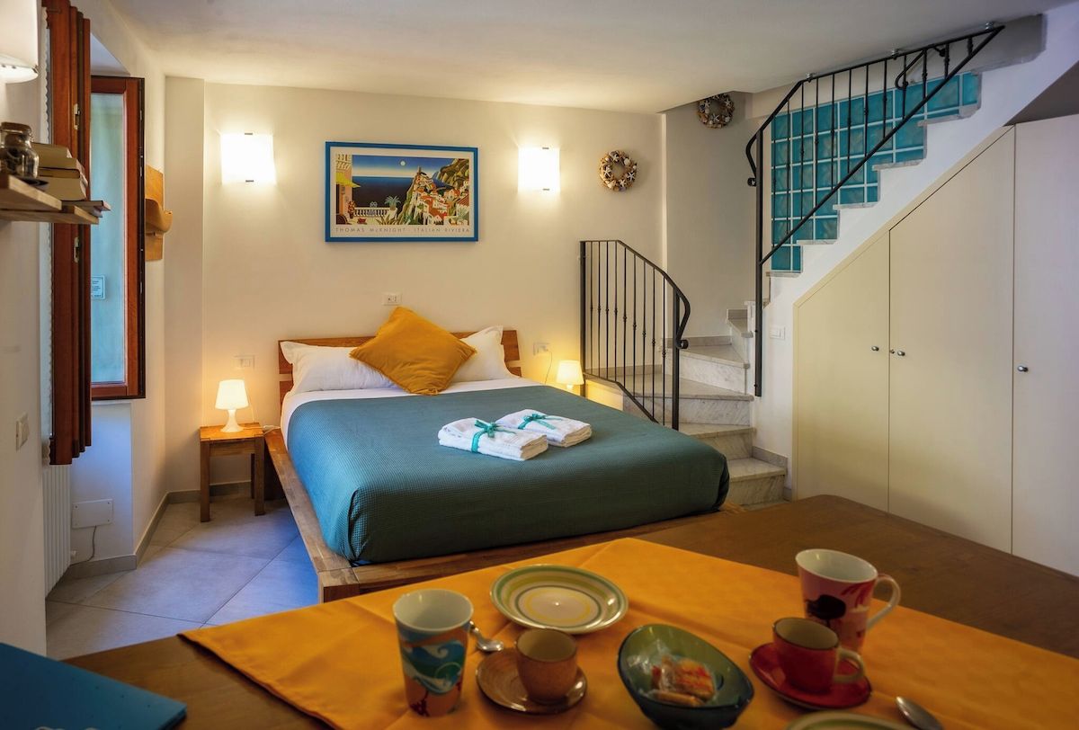 A hotel room with a bed, a table with breakfast items, a staircase, and a wall with a framed picture.