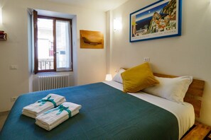 Quarto de hotel com cama, janela, quadro fixado na parede e radiador.