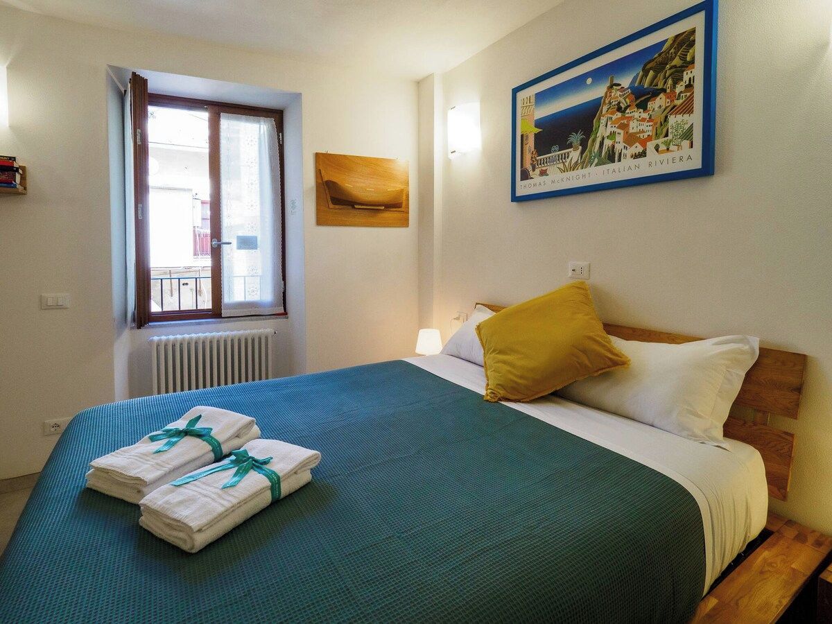 A hotel room with a bed, a window, a painting, and a radiator.