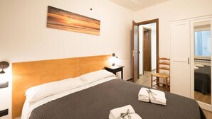 Quarto de hotel com uma cama, mesa de cabeceira, cadeira, guarda-roupa e um quadro na parede.