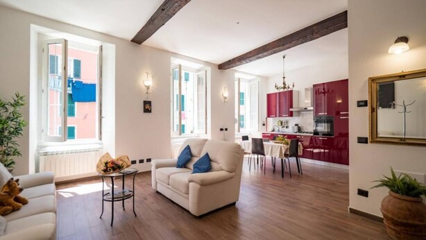 Sala de estar com um sofá, uma mesinha com um vaso, e um espaço de jantar com cadeiras.