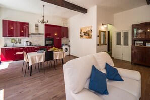 A modern kitchen with red cabinets, a dining table, and a white sofa with blue cushions.