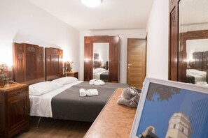A hotel room with a bed, a wooden wardrobe, a bedside table with a lamp, and a framed picture on the wall.