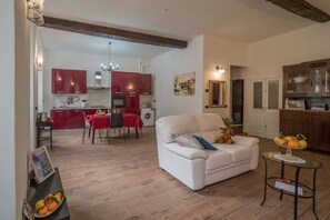 Un salon avec un canapé blanc, une petite table ronde sur laquelle on a disposé des fruits, et un coin repas avec une nappe rouge.