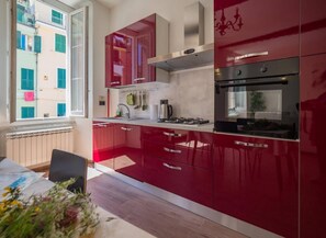 A modern kitchen with red cabinetry, a gas stove, and a built-in oven. - Tedea 2-Bedroom 2-Bathroom Exclusive Apartment (Vernazza)