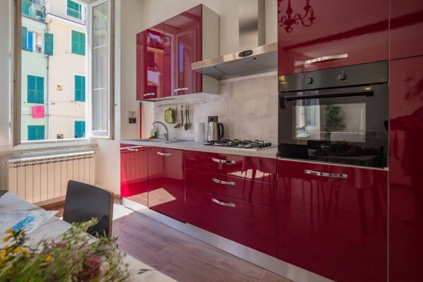 A modern kitchen with red cabinets, stainless steel appliances, and a window overlooking a building.