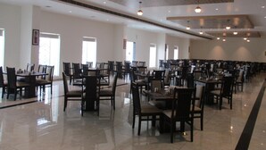 Un comedor amplio con varias mesas y sillas, techos altos e iluminación colgante.