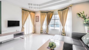 A modern living room with a flat-screen TV, a sofa, a coffee table with a plant, and curtains. - OYO 926 Sydney Resort (Si Prachan)