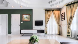 A modern living room with a flat-screen TV, a white entertainment unit, and a decorative plant on a marble coffee table. - OYO 926 Sydney Resort (Si Prachan)