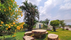 A garden with large stone tables, a palm tree, and a building in the background. - OYO 926 Sydney Resort (Si Prachan)