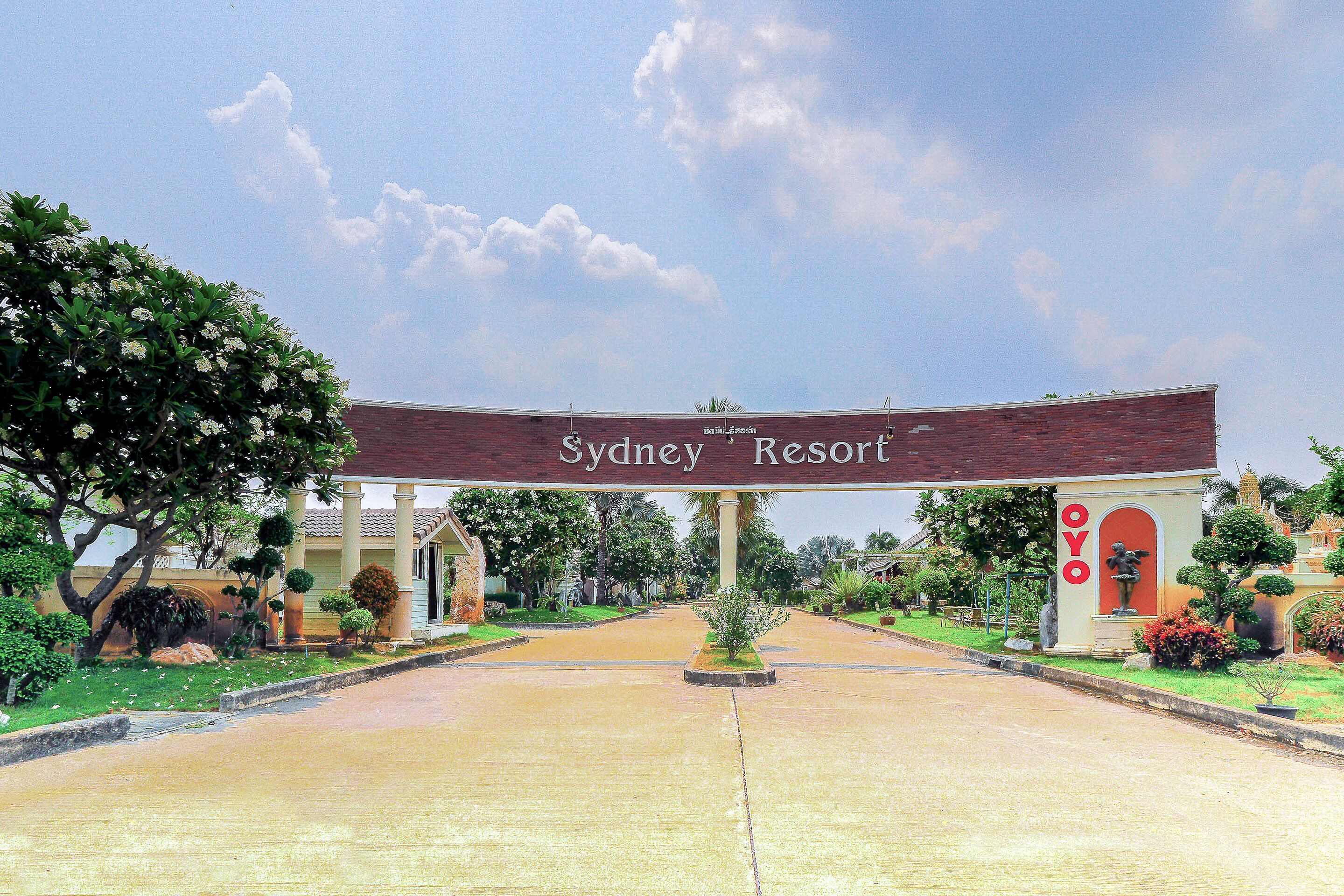 The entrance to Sydney Resort with a clear pathway leading to the main building, surrounded by well-maintained landscaping and a prominent sign.