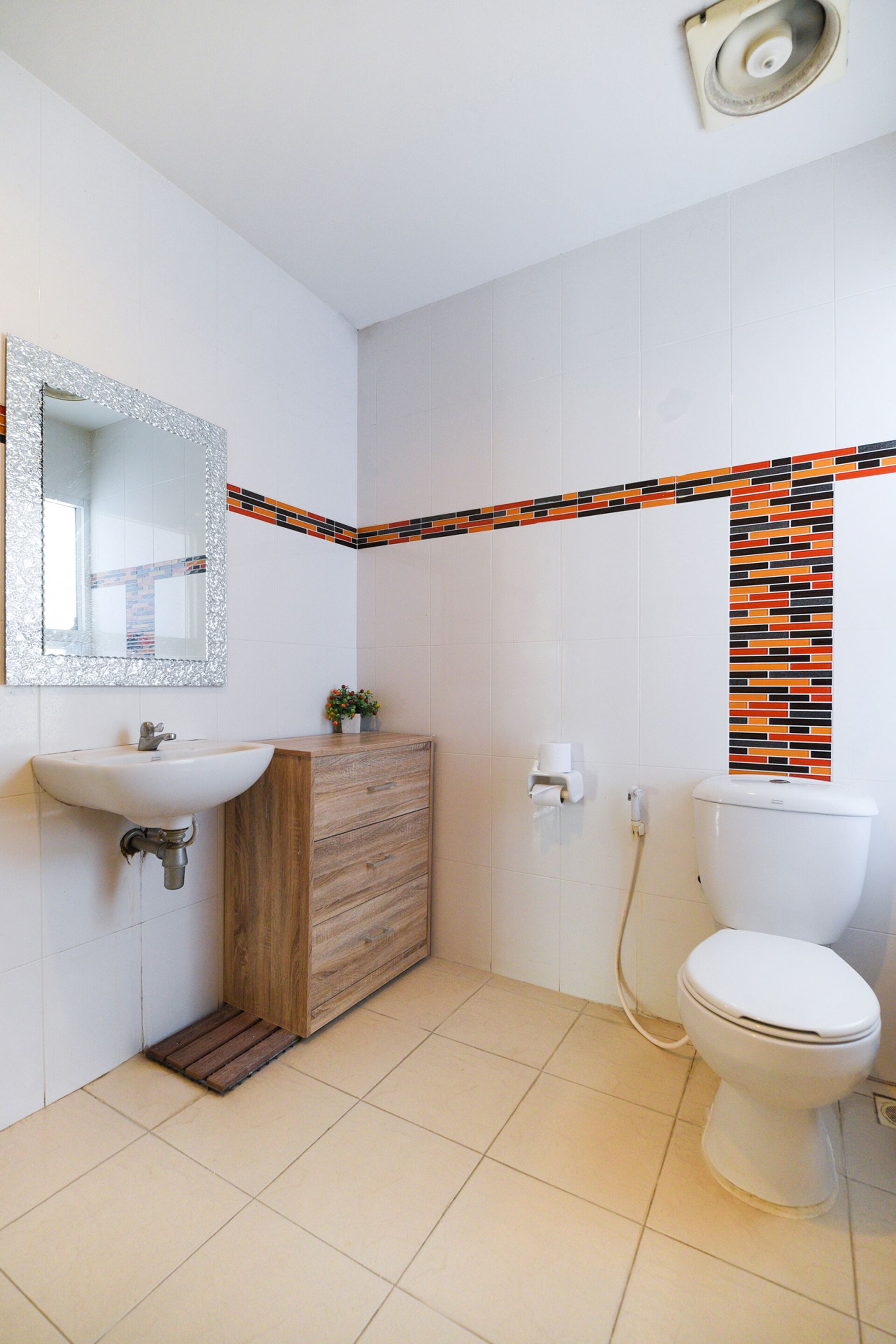 A bathroom with a white sink, wooden vanity, a mirror with a silver frame, a toilet, and a tiled floor.