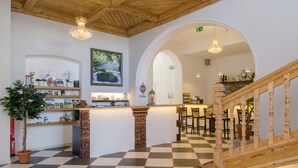 Un vestíbulo con piso a cuadros, escalera de madera y mostrador de recepción con planta y cuadros enmarcados.